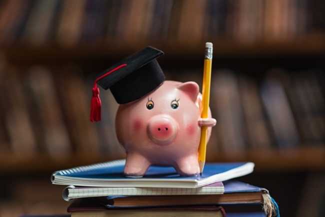 Piggy bank wearing a graduation cap standing on a stack of books